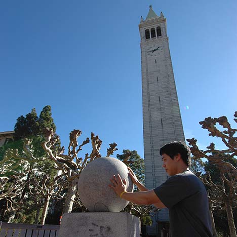 Student touching a stone ball with Campanile in background