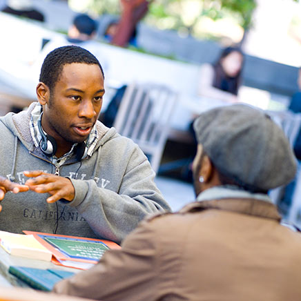 Two black students having a discussion at outdoor table.