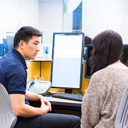 Male in front of computer speaking to student beside him.