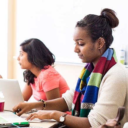 Two women sitting at table in front of laptops