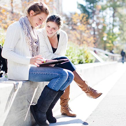 Two females sitting on a short wall looking at a hand held device