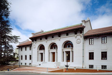 White building with red tile and copper roof and three arched doorways.