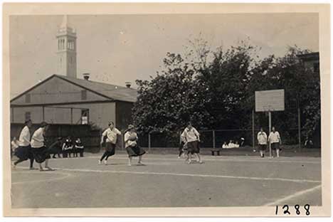 Historic black and white photo of young women playing basketball.