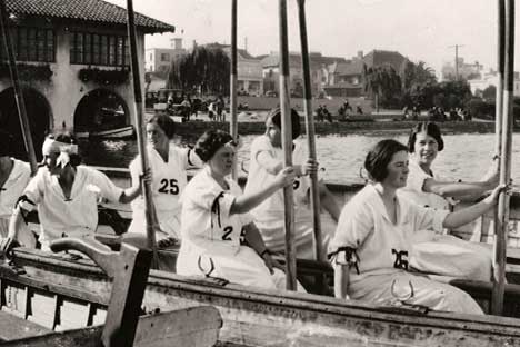 Historic black and white photo of young women in boats with oars.