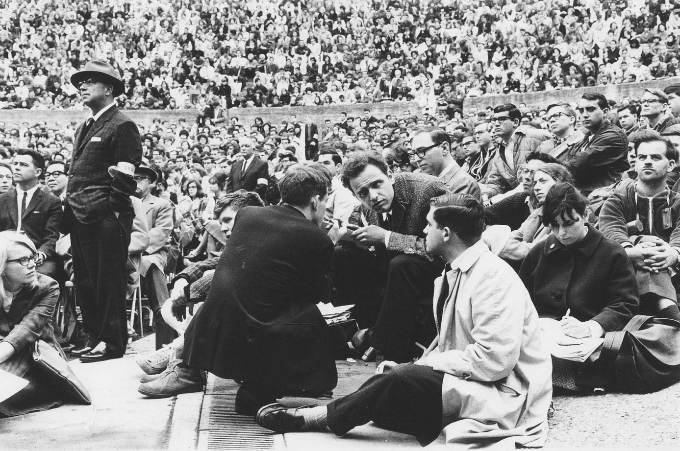 Mario Savio in the Hearst Greek Theater. Bettina Aptheker is sitting behind Savio. Sidney Stapleton sitting in front.