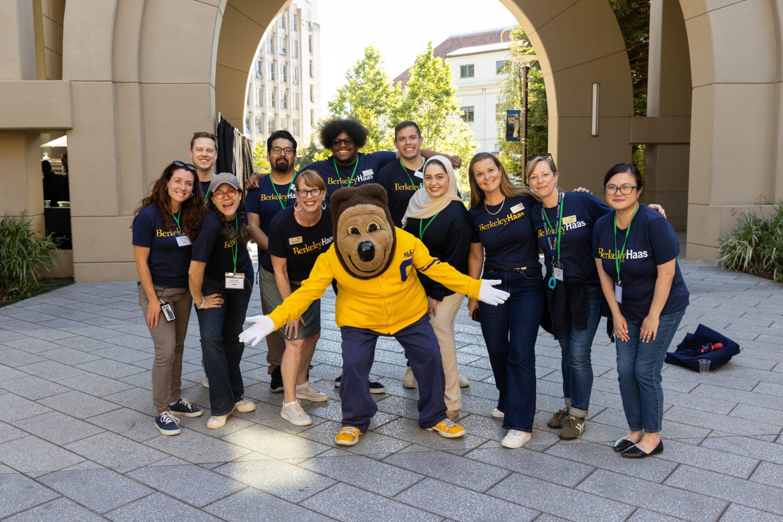 group of men and women stand in front of the arch at Haas Berkeley with shirts that read: Berkeley Haas. Oski the bear stands in front with arms open