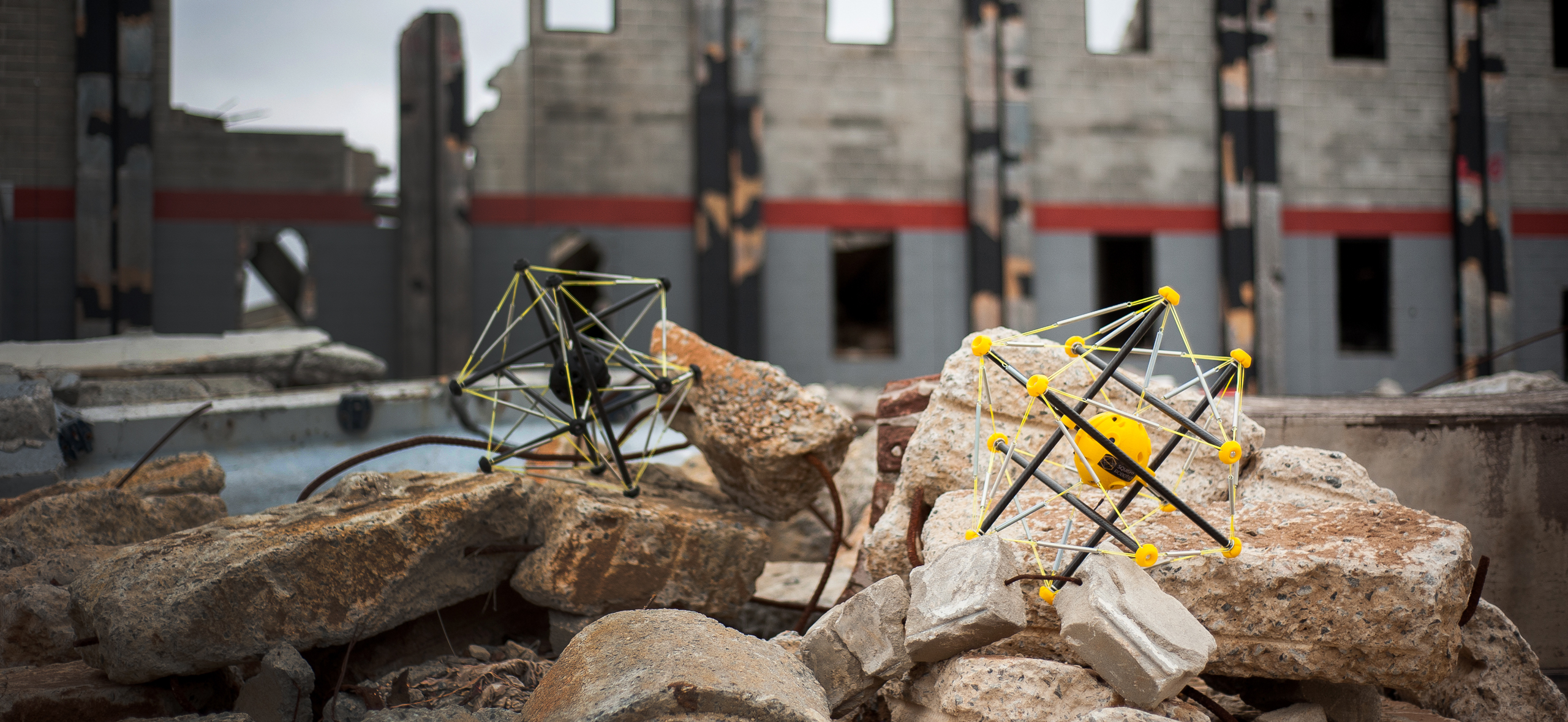 pile of rocks with two small robots on top, with a building in the background