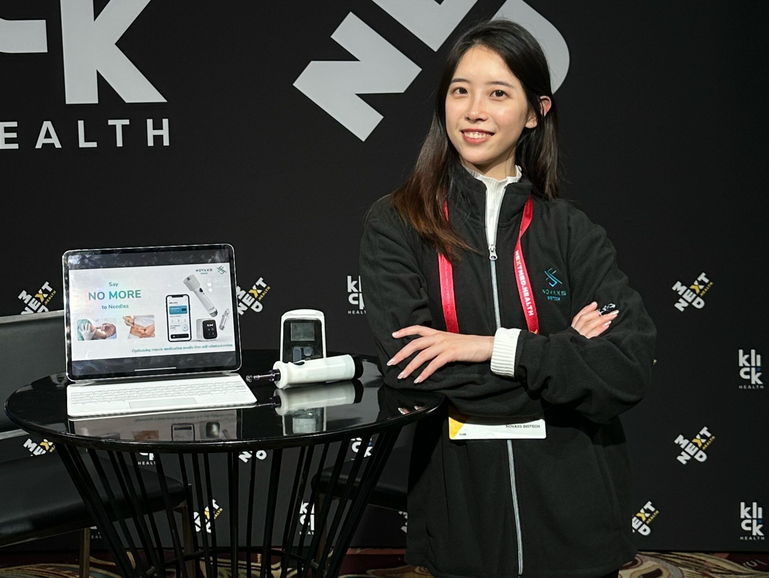 Alina Su stands next to a table with a laptop and medical device on it