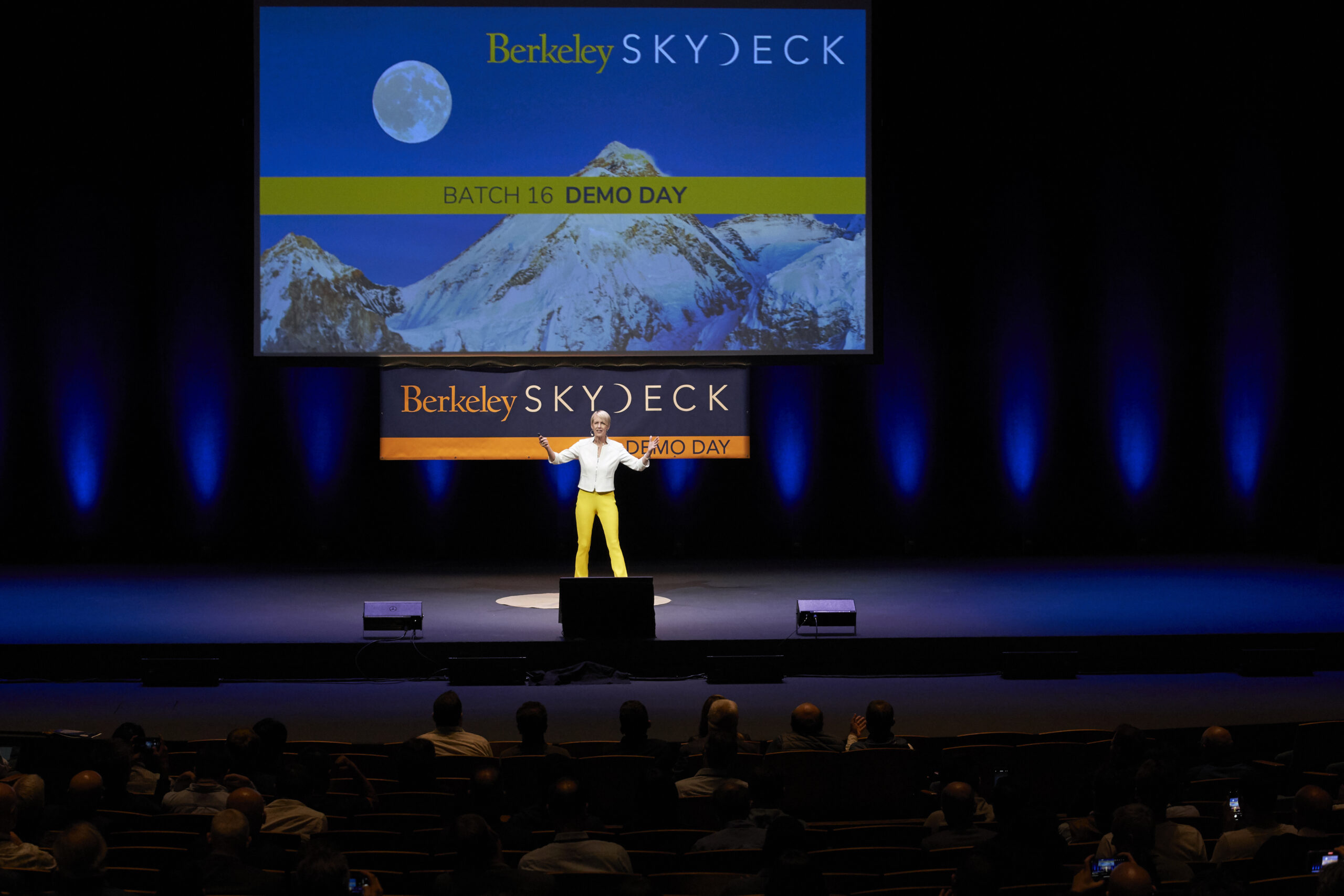 woman stands on stage with a large screen behind her that says 