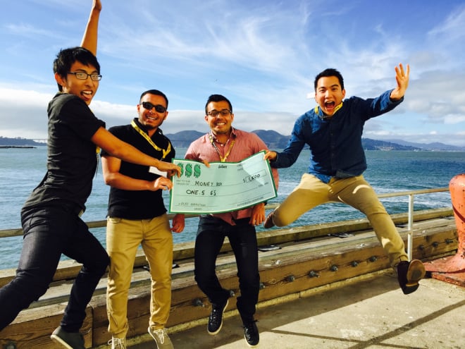 four young men hold an oversized check - two of the men are jumping and two are standing