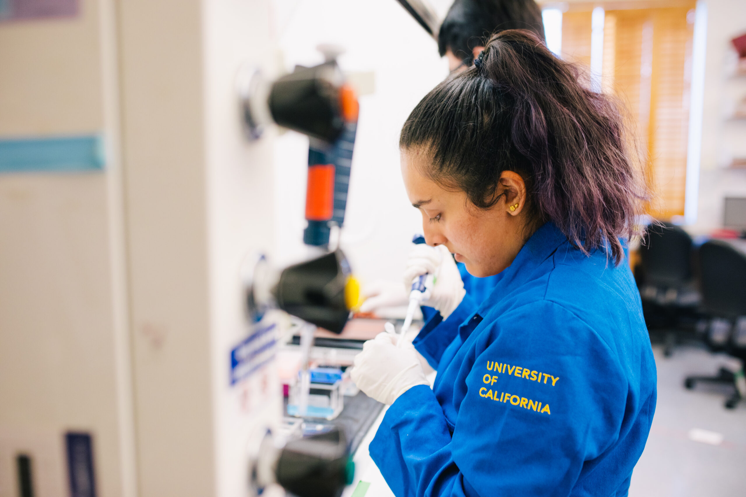 A scientist wearing a blue lab coat that reads